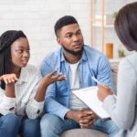 Young couple about to be married with relationship problems sitting at therapy session with psychologist